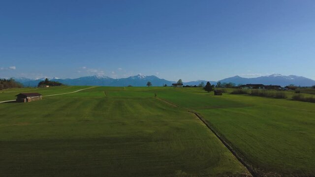Scenic 4K aerial view upon Bavaria's famous lake Chiemsee in the rural countryside with a beautiful blue sky and the alps mountains in the background, green lush fields lead up to the shore in spring