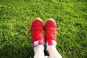 Woman sits on the grass, female legs in red sneakers on a background of green grass