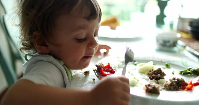 Little baby boy spitting food into plate during meal. Child spits food