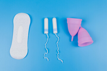 Sanitary pad, tampons and menstrual cup on blue background. Top view. Concept of critical days, menstruation, feminine hygiene