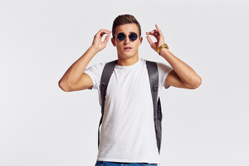 Fototapeta premium man in sunglasses with a backpack on his back and in a white t-shirt on a light background cropped view of emotion