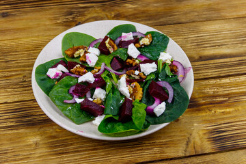 Tasty spinach salad with boiled beetroot, feta cheese, walnut and red onion on wooden table. Healthy vegetarian food