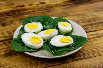 Boiled eggs with fresh spinach leaves and sesame seeds on wooden table