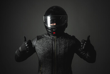 A happy motorbiker in helmet is showing a thumbs up gesture on a dark background.