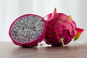 Dragon fruit sliced into 2 pieces with one piece facing back on a wooden table.