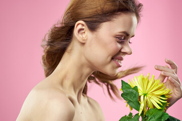 Beautiful woman with naked shoulders and a yellow flower in her hands on a pink background