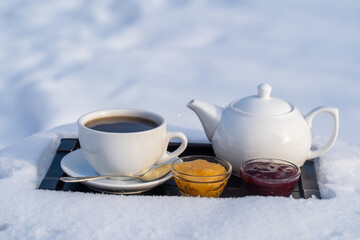 White cup of hot tea and teapot on a bed of snow and white background, close up