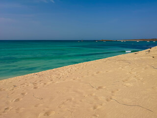 Colorful Atlantic Ocean and sandy beach on the island of Boa Vista, Cape Verde. Tropical climate and hot winter day. Selective focus on the footstep pattern, blurred background.