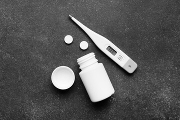 Electronic thermometer with pills on dark background