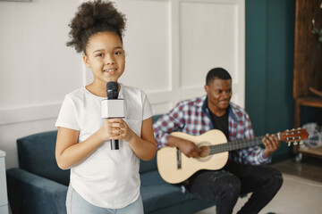 Dad is sitting with a guitar and daughter with a microphone