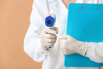 Doctor with infrared thermometer on color background, closeup