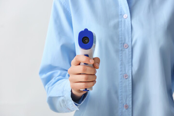 Woman with infrared thermometer on light background, closeup