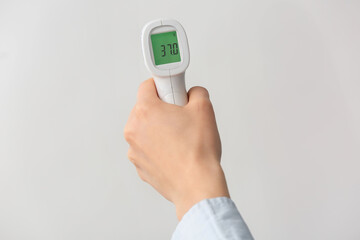 Female hand with infrared thermometer on light background