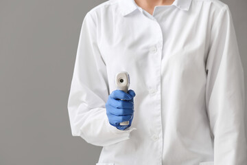 Doctor with infrared thermometer on grey background, closeup
