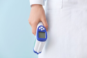 Doctor with infrared thermometer on color background, closeup