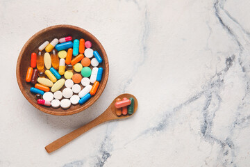 Bowl and spoon with different pills on light background