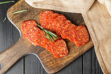 Board with tasty salami on dark wooden background