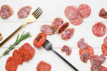 Composition with slices of different sausages on white wooden background