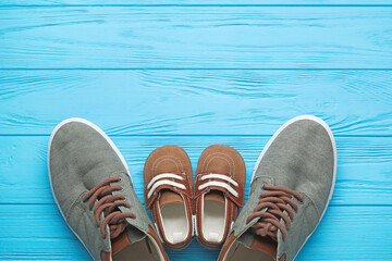 Naklejka premium Parent and child shoes on blue wooden background, family concept with adult sneakers and baby footwear, top view with copy space