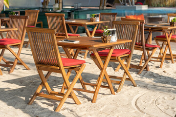 Wooden table and chairs in empty beach cafe next to sea. Close up, Thailand