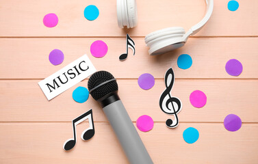 Microphone with headphones, music notes and confetti on color wooden background