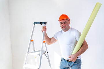 a repairman in a construction helmet with a toy with a roll of wallpaper holding one hand on a stepladder