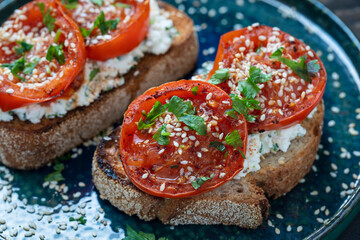 Delicious toasted bread with roasted red tomatoes, feta cheese, sesame seeds and herbs on plate