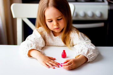 Little girl paints her nails with pink nail polish. Cute toddler girl  playing with colorful nail polish doing manicure. Cosmetics and beauty concept.