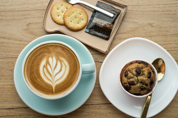 Close-up of Hot coffee latte with latte art milk foam in cup mug and Homemade Banana cup cake,biscuits on wood desk office desk in coffee shop at the cafe,Morning snack concept
