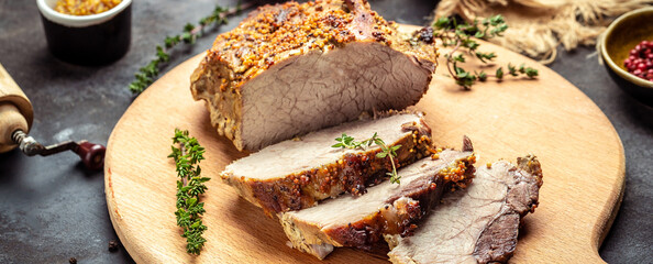 Close-up of sliced roast pork with thyme herb mustard on a cutting board. Restaurant menu, dieting,...