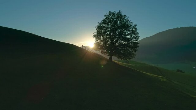 A silhouette of two people jogging up a hill as a bright sun sets in the distance behind them - Twilight