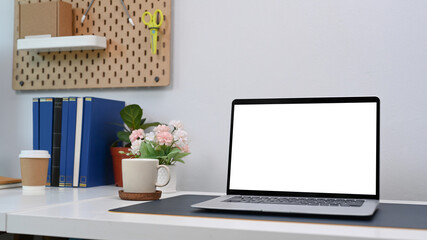 Close up view of mock up computer laptop with blank screen and office supplies on white desk in home office.