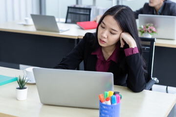 Upset thoughtful Young Asian business woman stress in the workplace working with laptop computer of Office staff are not happy in with working colleagues behind in the office