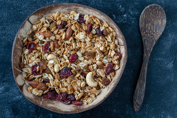Granola with oatmeal, dried fruit, honey, raisins, dry cranberry, almond and cashew nuts in a coconut bowl, close up