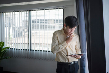 Fototapeta premium Young businessman standing in office room and reading news on digital tablet.