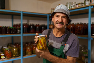 Man satisfied with the result of his work. He holds a glass jar with marinated peppers. Fermented organic food.