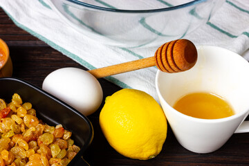 Honey in a cup, lemon, chicken egg and raisins on the kitchen table. Ingredients for making honey dough.