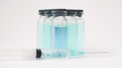 Vial vaccine, glass ampoules with transparent and blue liquid, a syringe is lying near on white background, global vaccination concept
