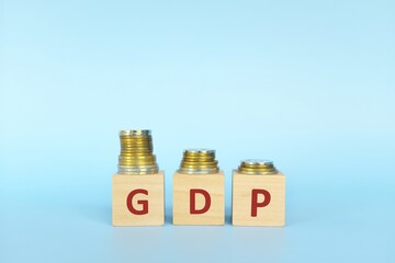 GDP or gross domestic product letters in wooden blocks with decreasing stack of coins. Economic crisis, decline and recession concept.