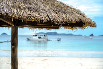 Umbrella hut seaside. Rustic hut wiht tourist boat floating on the sea at the background.