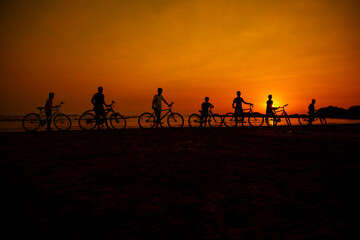 Silhouette of children standing by bicycle on the beach with beautiful sunset nature. Concept. friendly family.flare light.selected focus.group, children, team, bicycle.