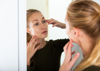Cheerful woman is concentrared looking on her face in the mirror at the home
