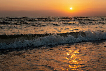 Colorful sunset on a sandy beach, waves with foam on the sand. Ocean, coast. Soft selective focus, defocus