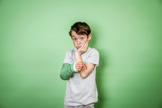 cool young schoolboy with broken arm and green arm plaster posing in front of green background