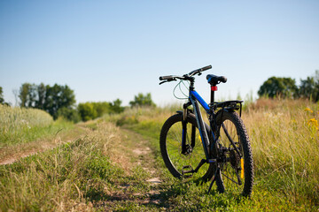 Fototapeta na wymiar bike stands on in the field. A mountain bike stands on a field path with green grass. cycling. Mountain bike. outdoor cycling activities. space for text. editorial, Ukraine, Kiev region 2020