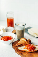 Breakfast with a fresh croissant and a cup of aromatic coffee latte, tangerine jam, butter and brie cheese. Fruit carving. Healthy breakfast.