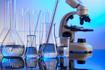 Coronavirus pandemic theme. Science research concerning fast covid tests and anti-covid vaccine. Microscope, beakers and test tubes on blue background.