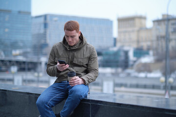 young man using smartphone and listens to music in bluetooth headphones. lonely man in autumn...