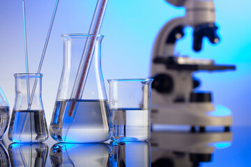 Coronavirus pandemic theme. Science research concerning fast covid tests and anti-covid vaccine. Microscope, beakers and test tubes on blue background.