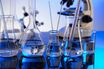 Coronavirus pandemic theme. Science research concerning fast covid tests and anti-covid vaccine. Microscope, beakers and test tubes on blue background.